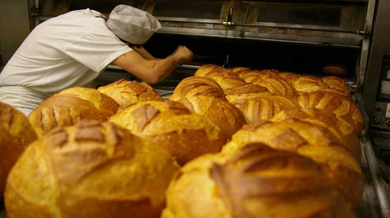 Bäcker holt Brötchen aus dem Ofen